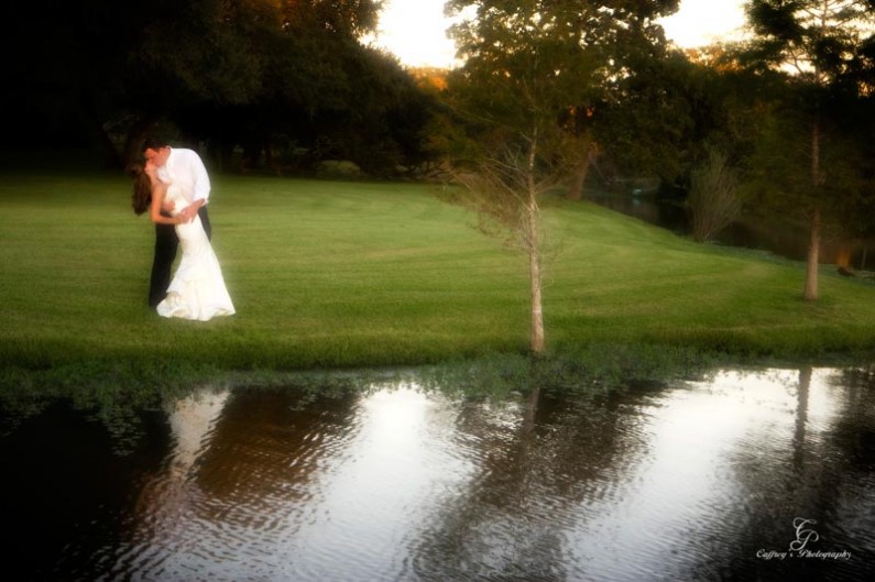 Bride and groom kissing by the lake at the Wedding venue in Columbus Tx called The Phoenix Rising. 