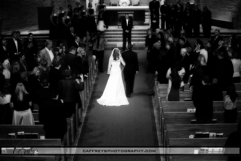 Bride and her father walking down the aisle toward her groom during their wedding at St Rose of Lima Catholic Church.