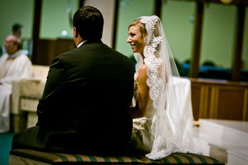 Bride smiling at the groom as they listen to the priest during their wedding. 